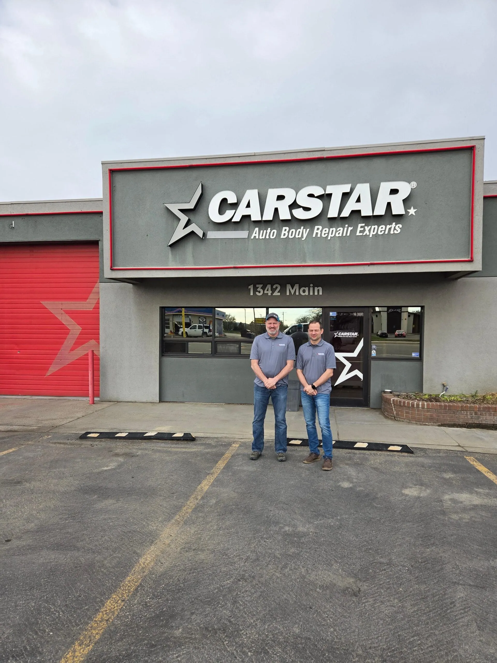 Two people standing in front of a CARSTAR collision repair shop