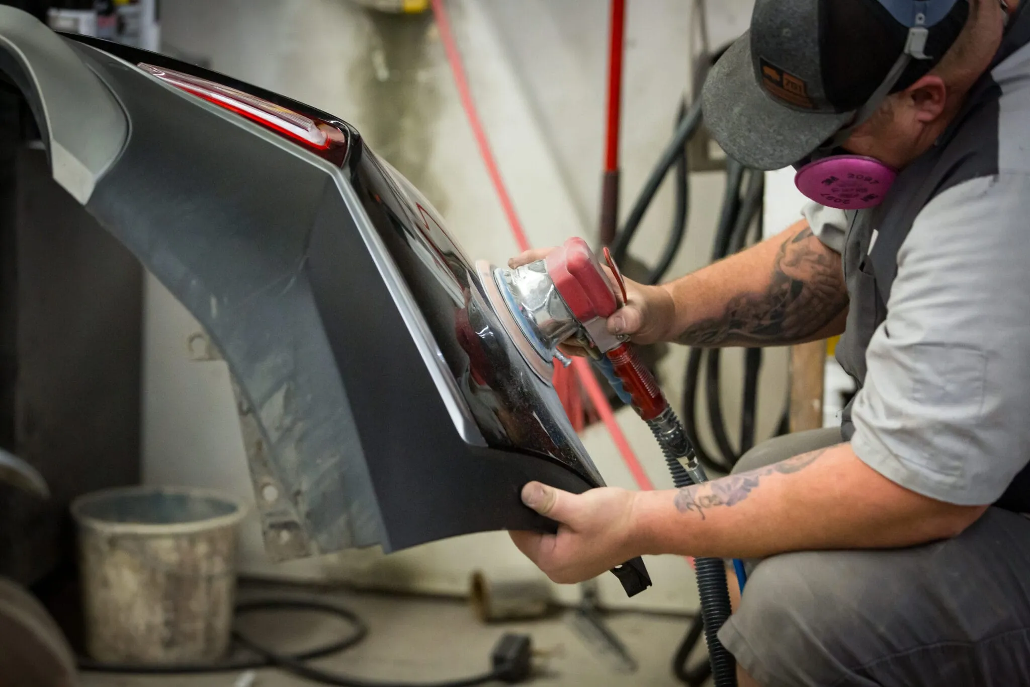 Technician in a respirator sanding a removed bumper cover