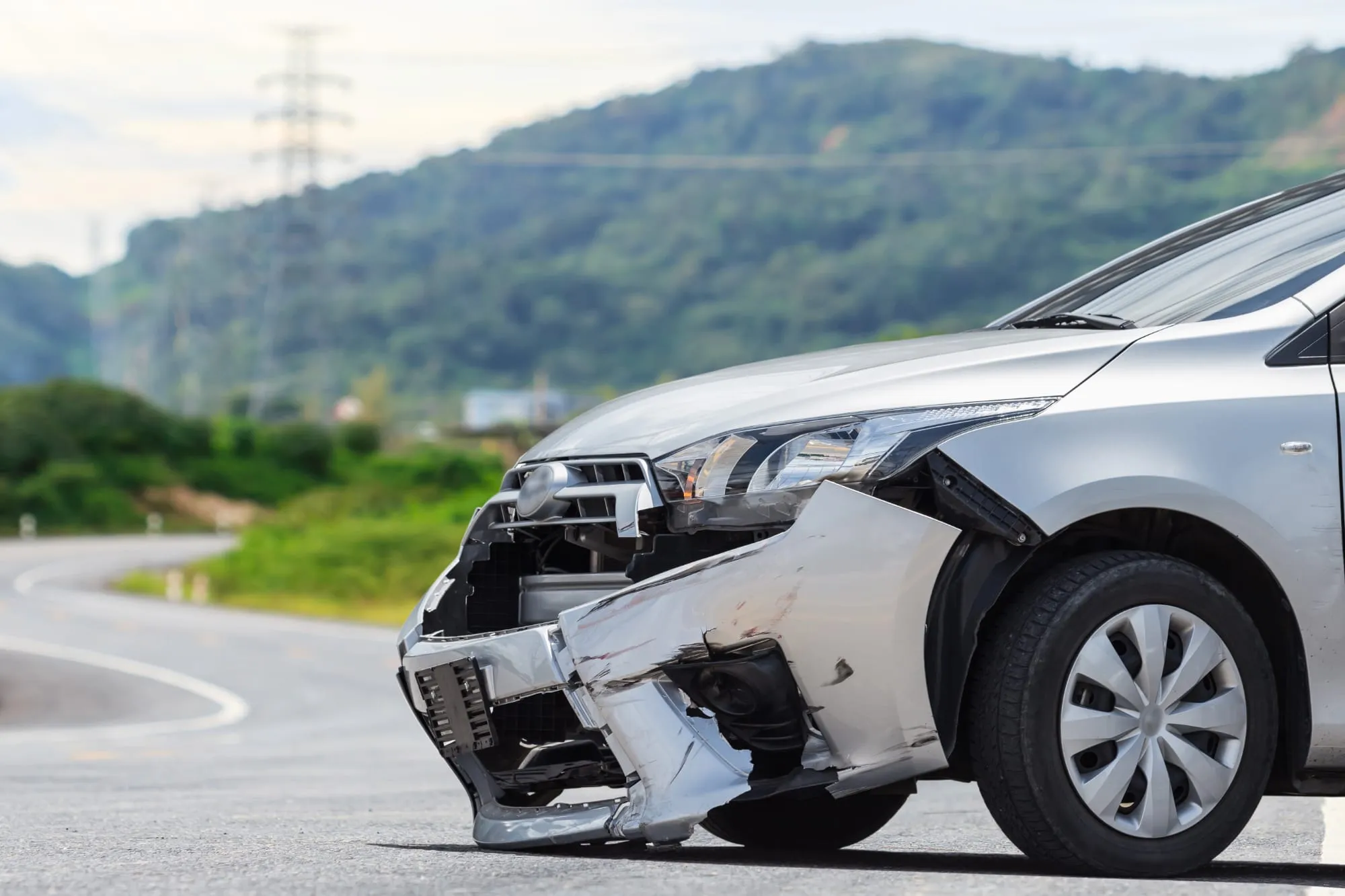 Grey car with a damaged front corner on a road with hills behind