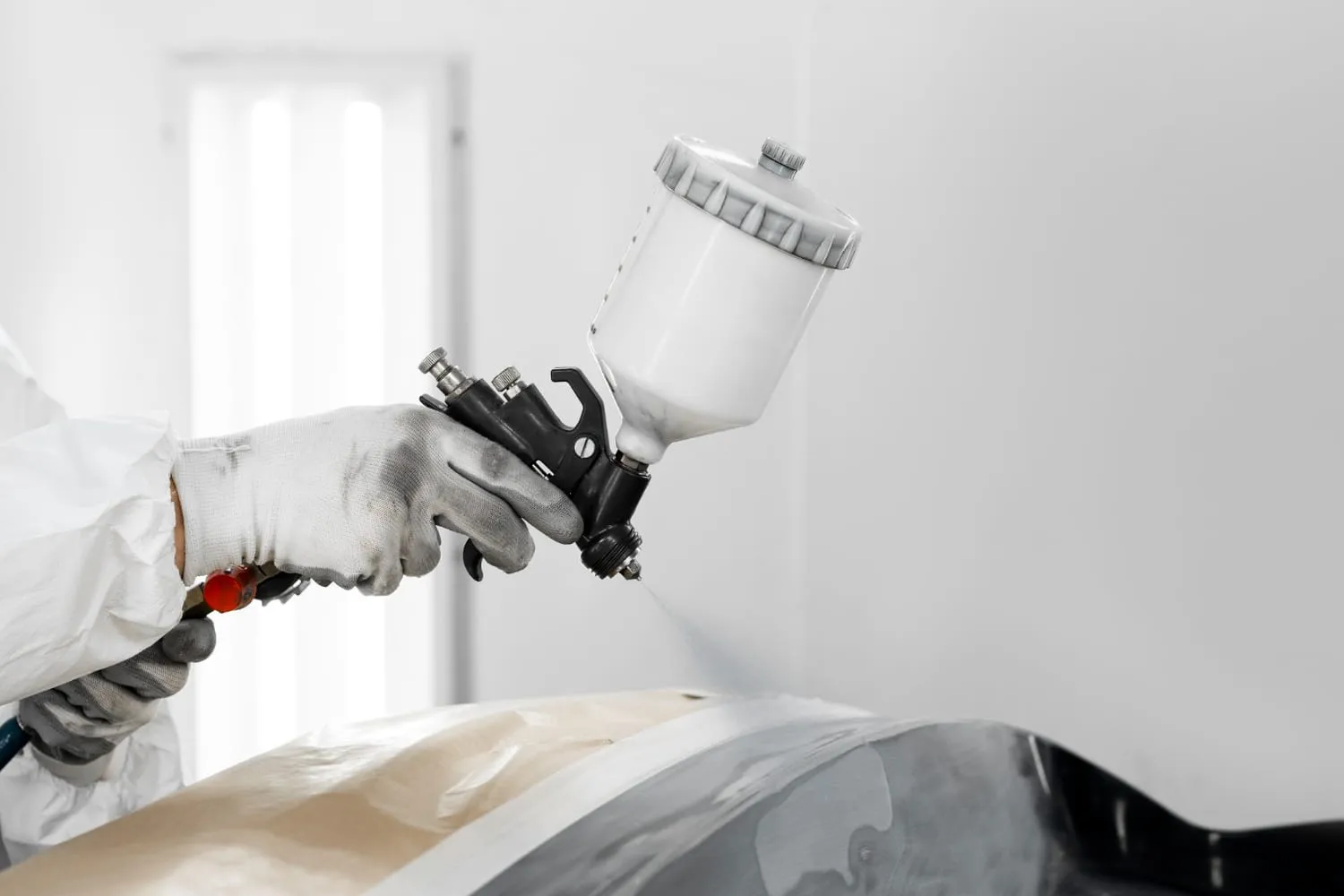 Gloved hand holding a paint spray gun over a panel