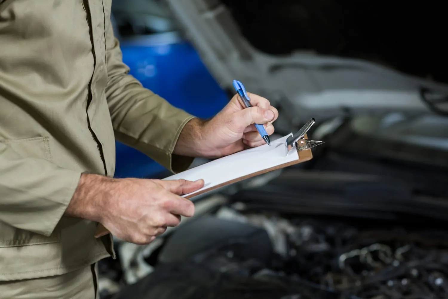 Estimator with a clipboard writing next to an open hood