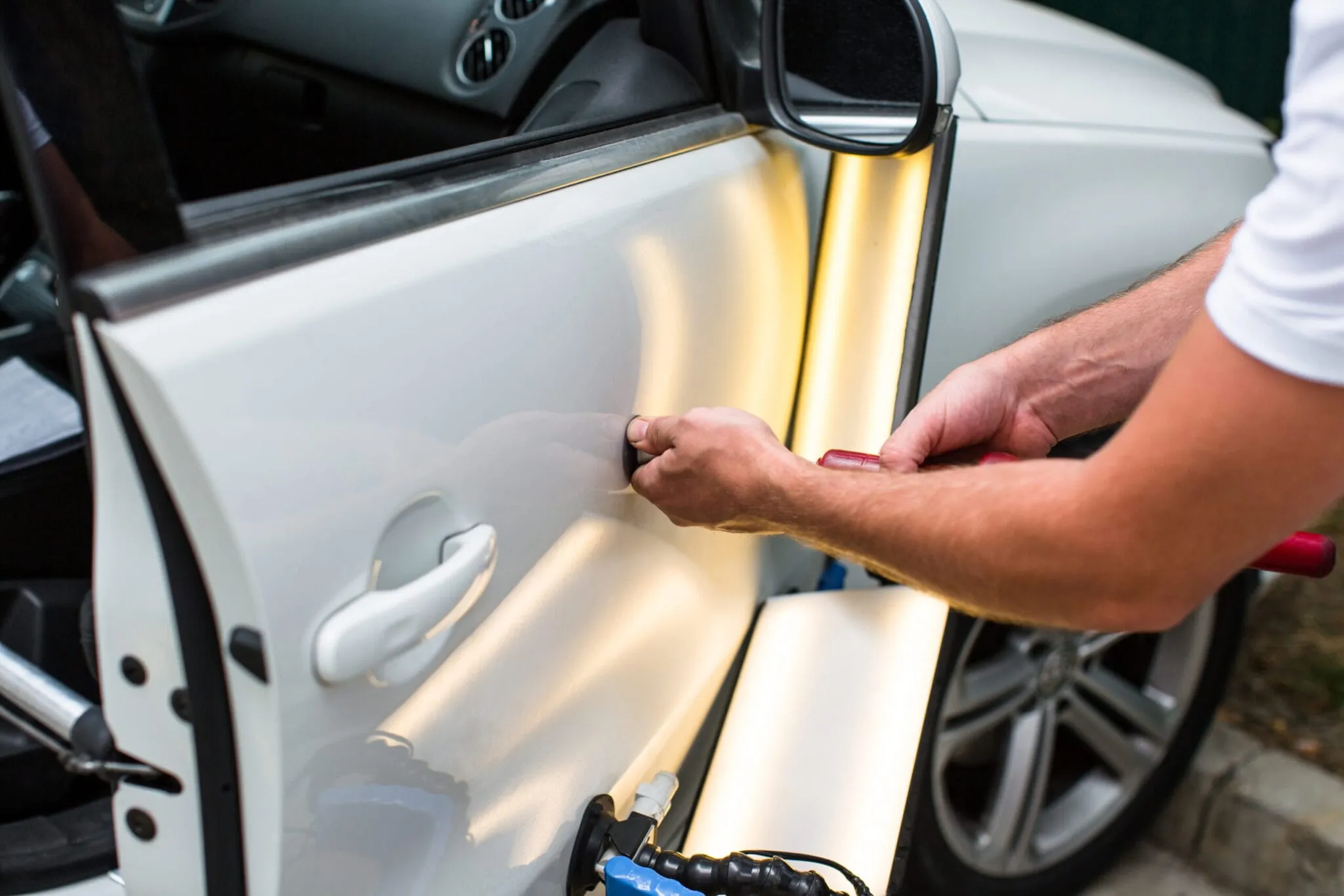 Hand using a dent-repair tool on a white car door