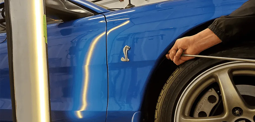 Hand using a long dent rod behind the blue fender of a car