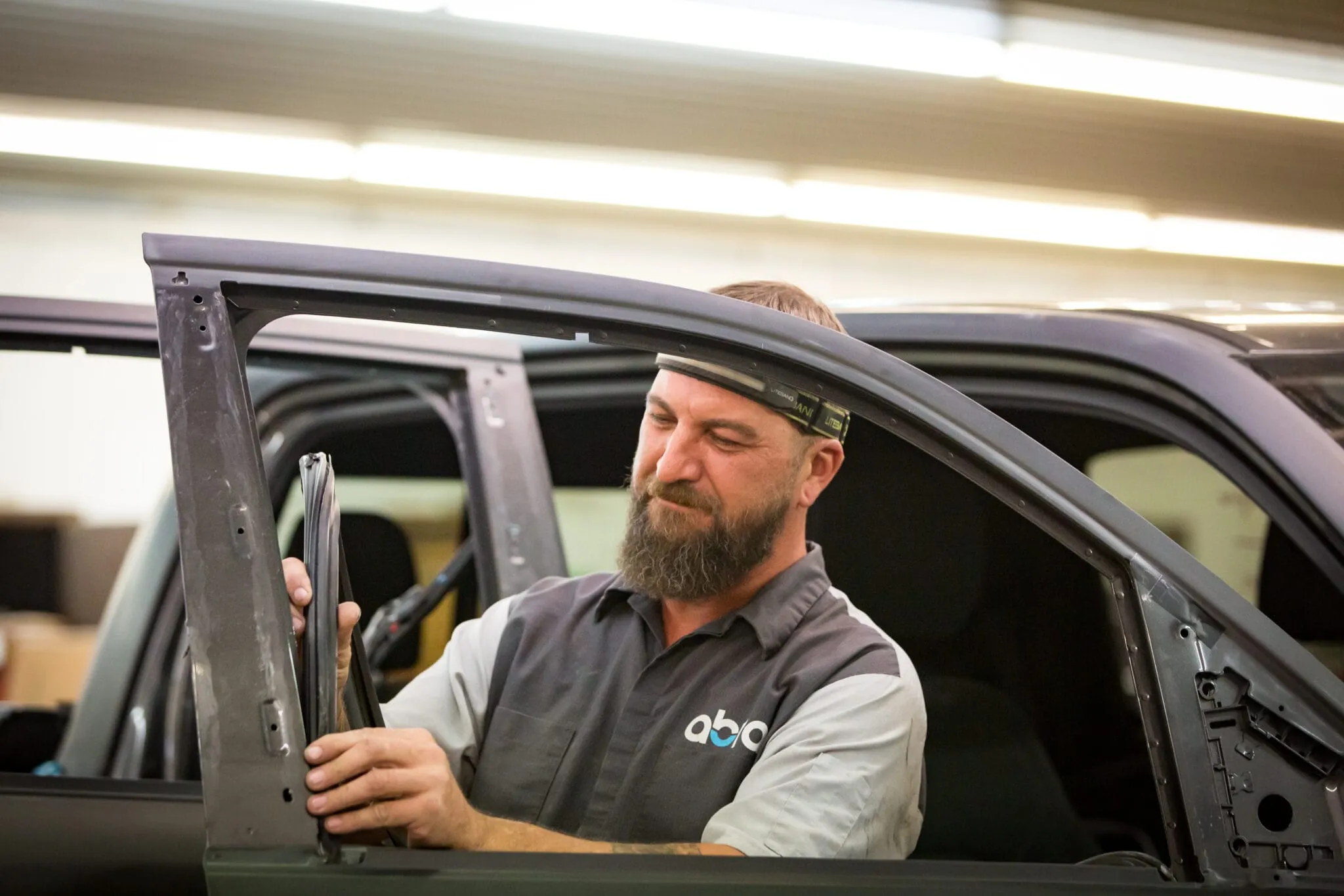 Bearded technician in an ABRA shirt leaning into a vehicle with its door open