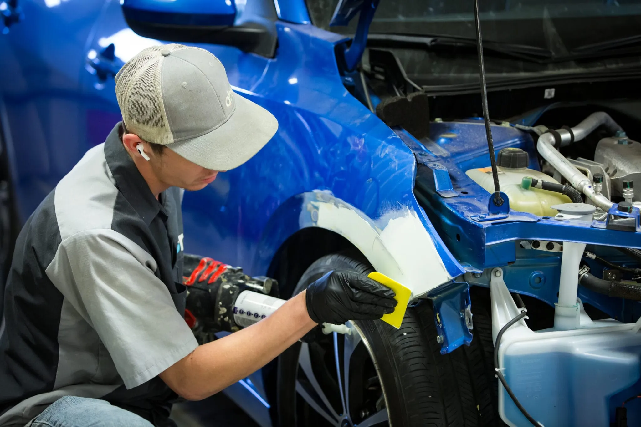 Technician in a cap sanding the fender of a blue car