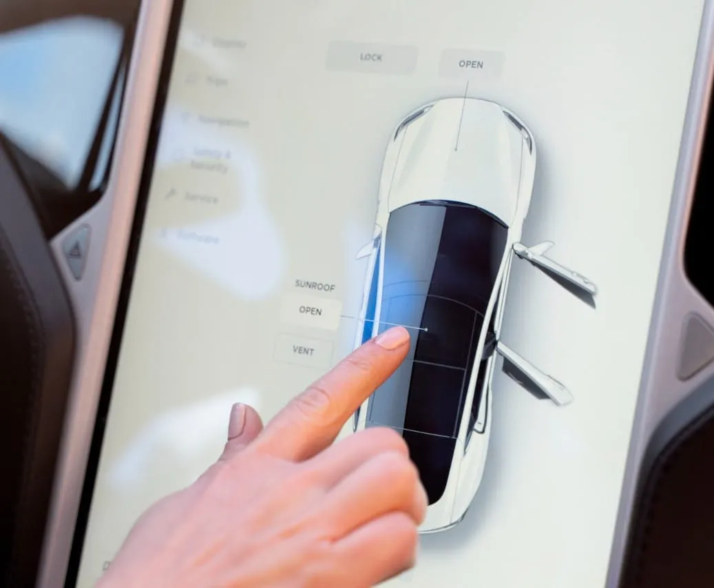 Hand touching a car-control touchscreen showing a top view of a vehicle